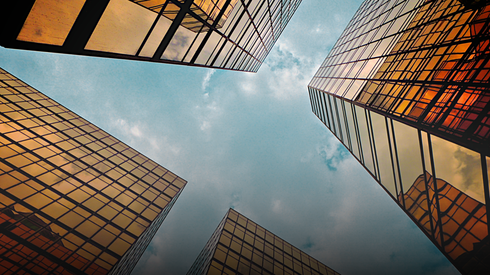 Looking up at tall gold-toned glass skyscrapers against a blue sky with clouds.