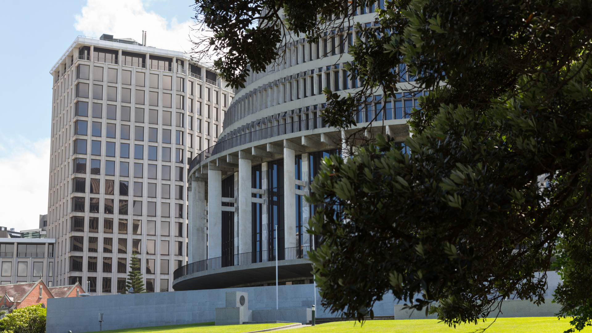 New Zealand Parliament buildings in Wellington, with a round Beehive building and a rectangular tower on a sunny day.