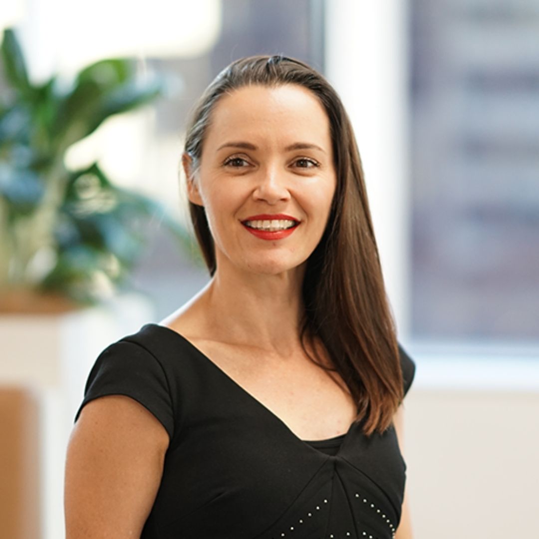 Woman with long brown hair, smiling, wearing a black dress.