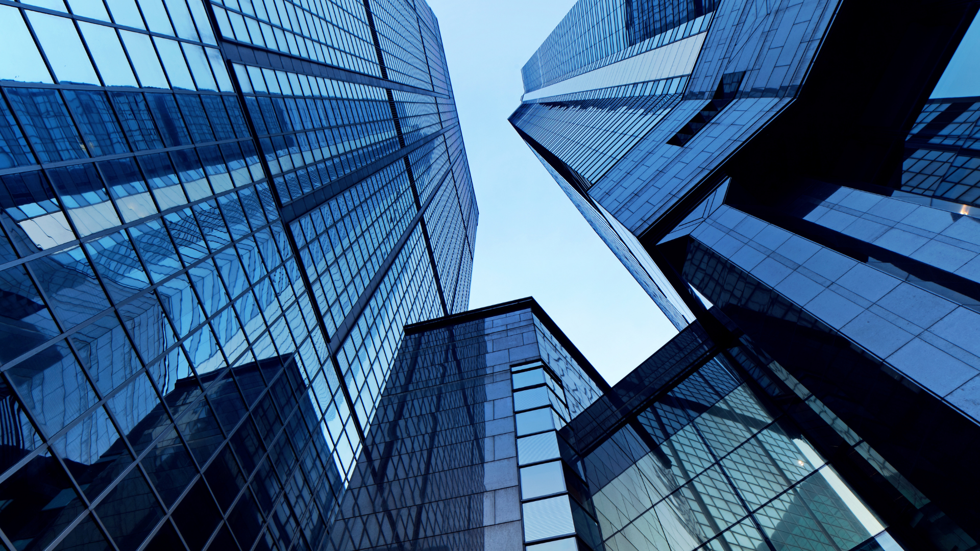 Low-angle shot of tall, modern skyscrapers with reflective blue-tinted windows against a bright sky.