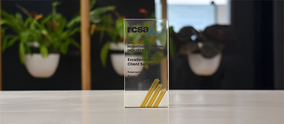 Transparent award on a white surface with text. Green plants are in the blurred background.