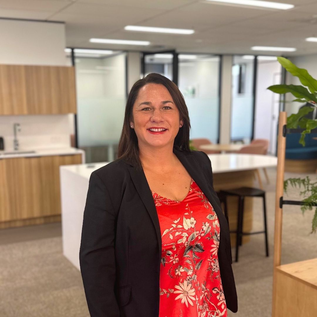 Woman in a red floral top and black blazer smiles in an office setting.