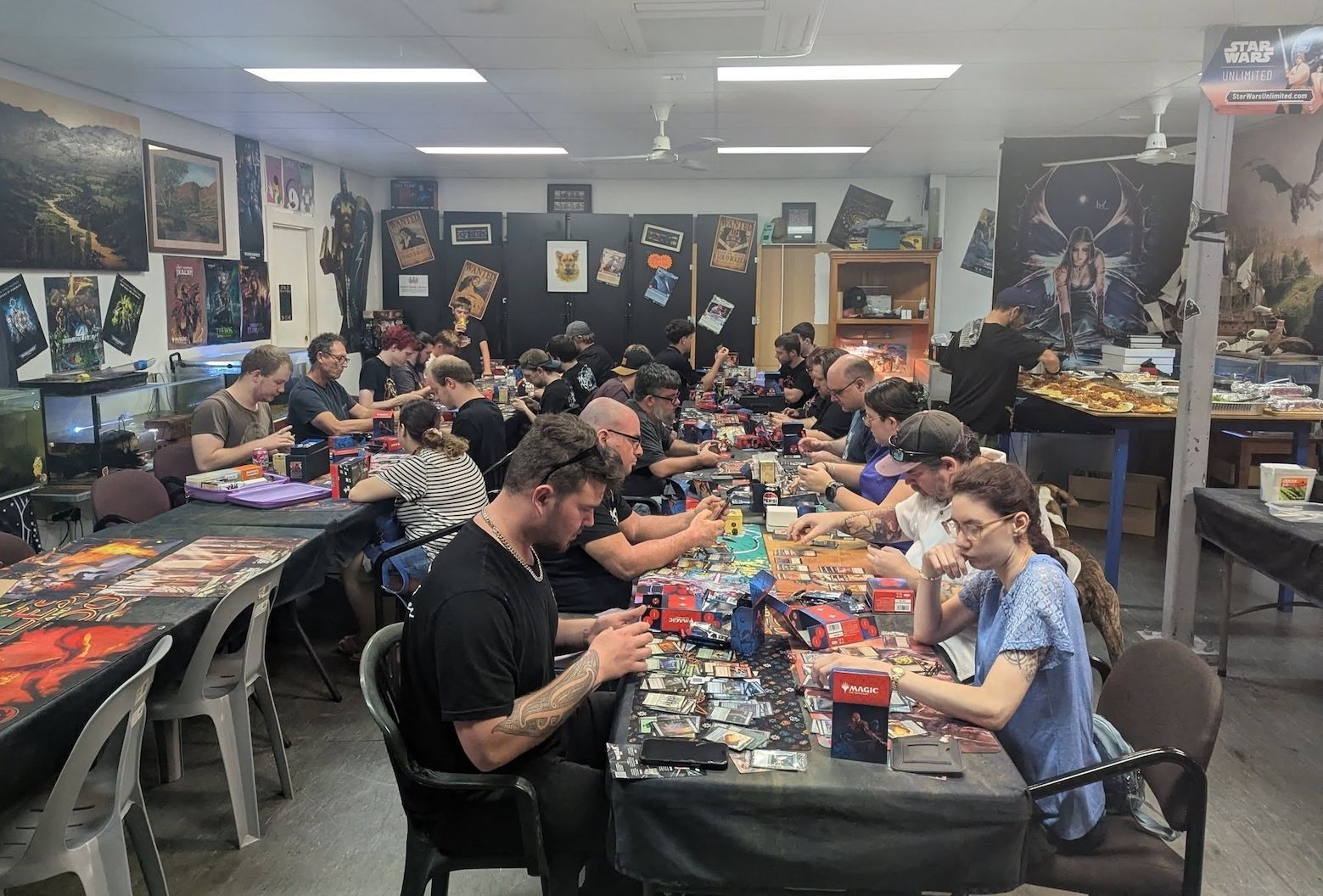 People seated at tables play games in a room with posters and decorations on the walls— Grim Gaming & Hobbies in Bundaberg Central, QLD