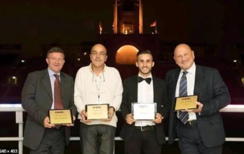 Quattro uomini in giacca e cravatta che tengono targhe davanti a un edificio