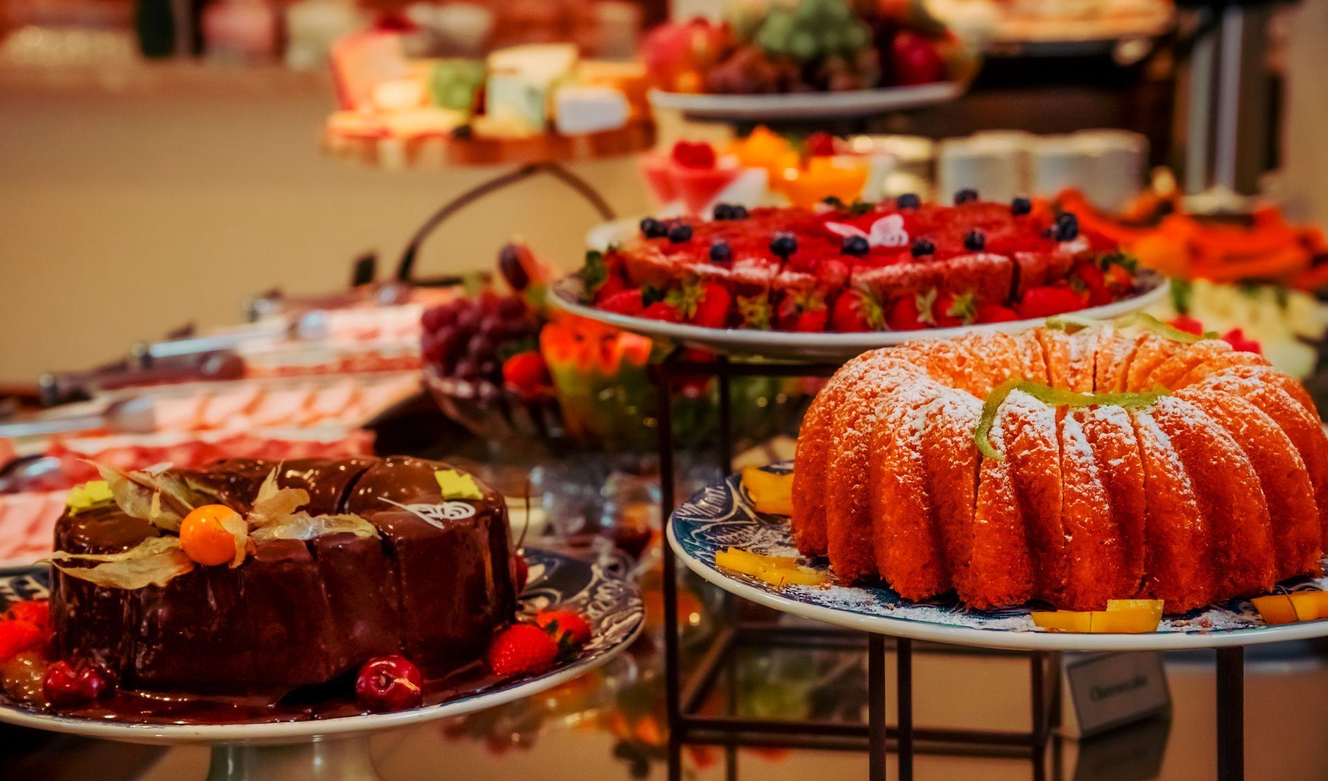 Um buffet de sobremesas com bolo de chocolate, torta de morango vermelha e bolo tipo bundt polvilhado com açúcar de confeiteiro.