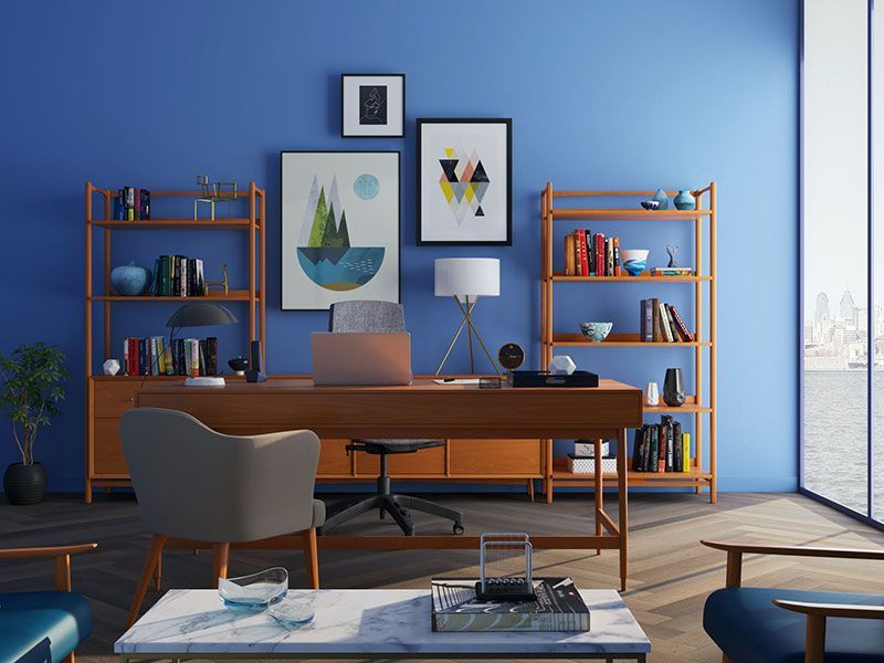 Escritório moderno em casa com mesa de madeira, duas estantes e obras de arte contra uma parede azul, com vista para a cidade.