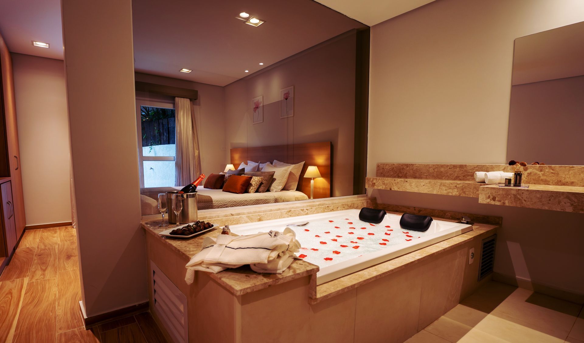 Um quarto de hotel com banheira de hidromassagem decorada com pétalas de rosa, posicionada em frente a uma cama king-size.