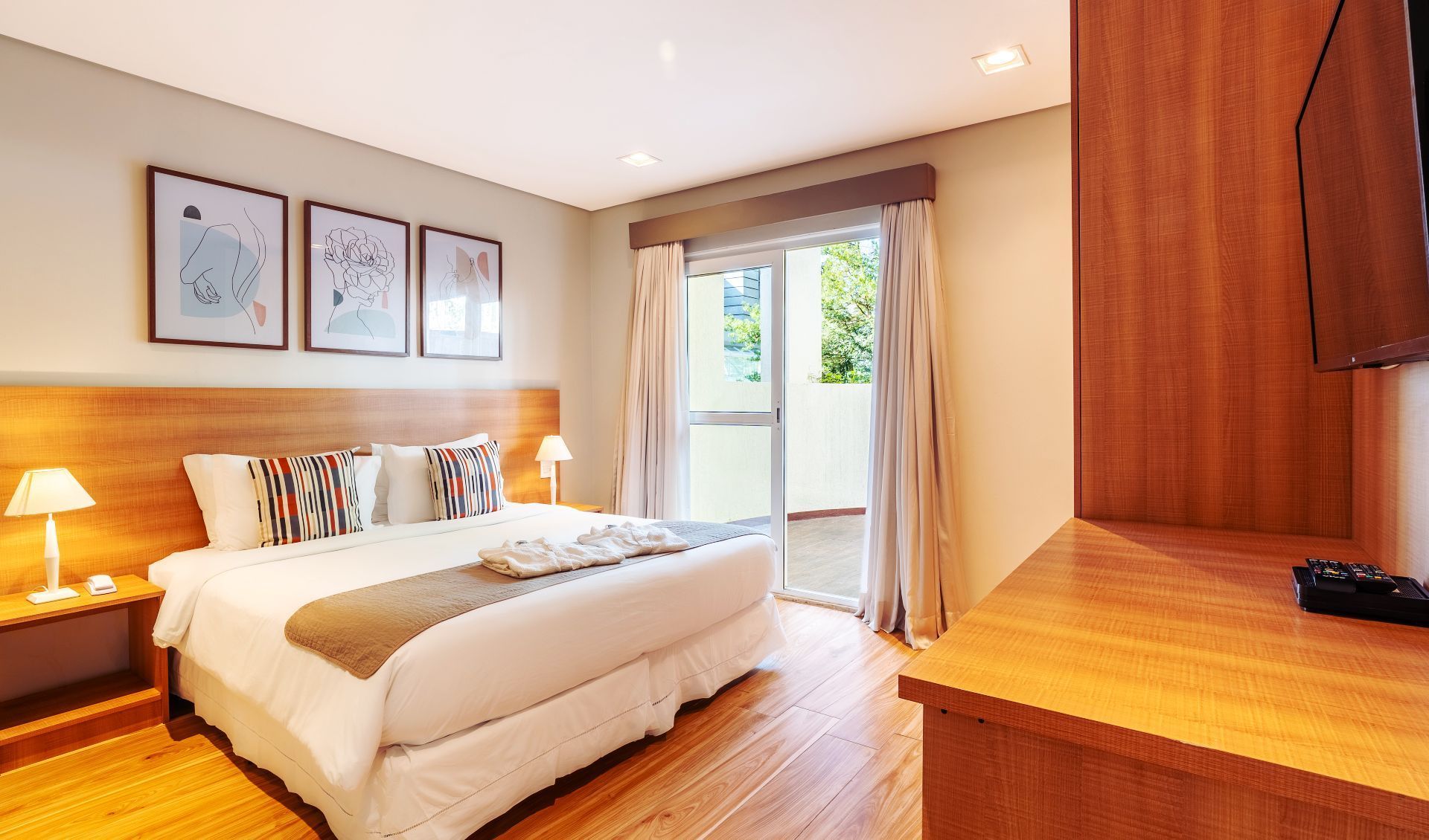 Um quarto de hotel com cama de casal, cabeceira de madeira, abajures, varanda e móveis de madeira.
