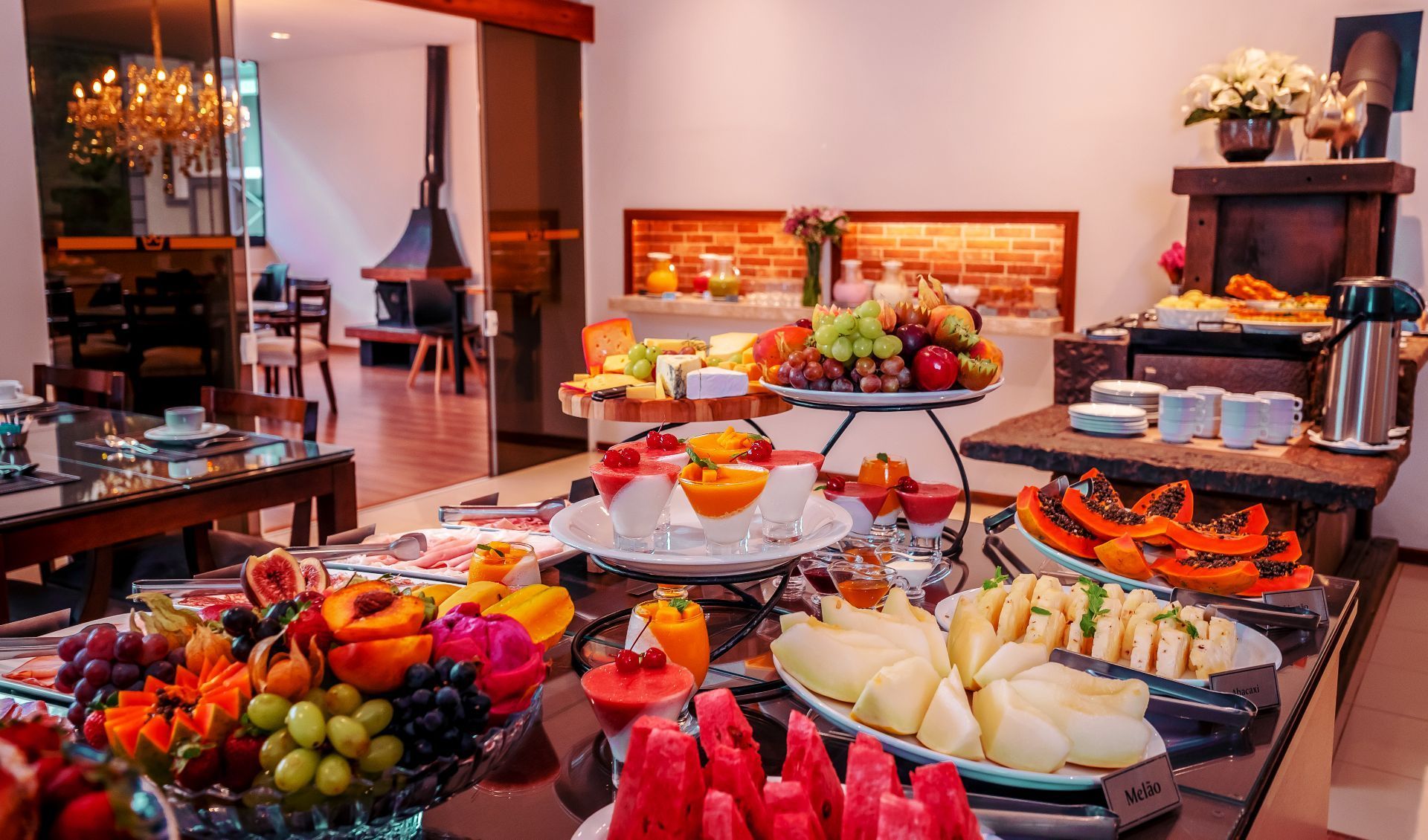 Um buffet de café da manhã com frutas frescas, pequenos parfaits e doces em uma área de refeições bem iluminada.