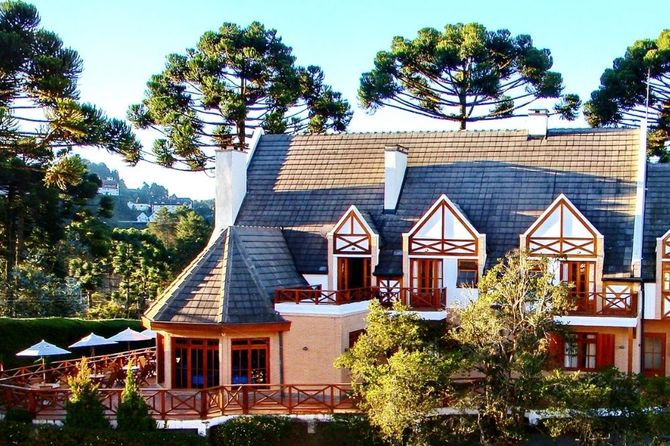 Um edifício de hotel em estilo europeu com telhado íngreme de telhas, detalhes em estrutura de madeira e um pátio externo rodeado por árvores.