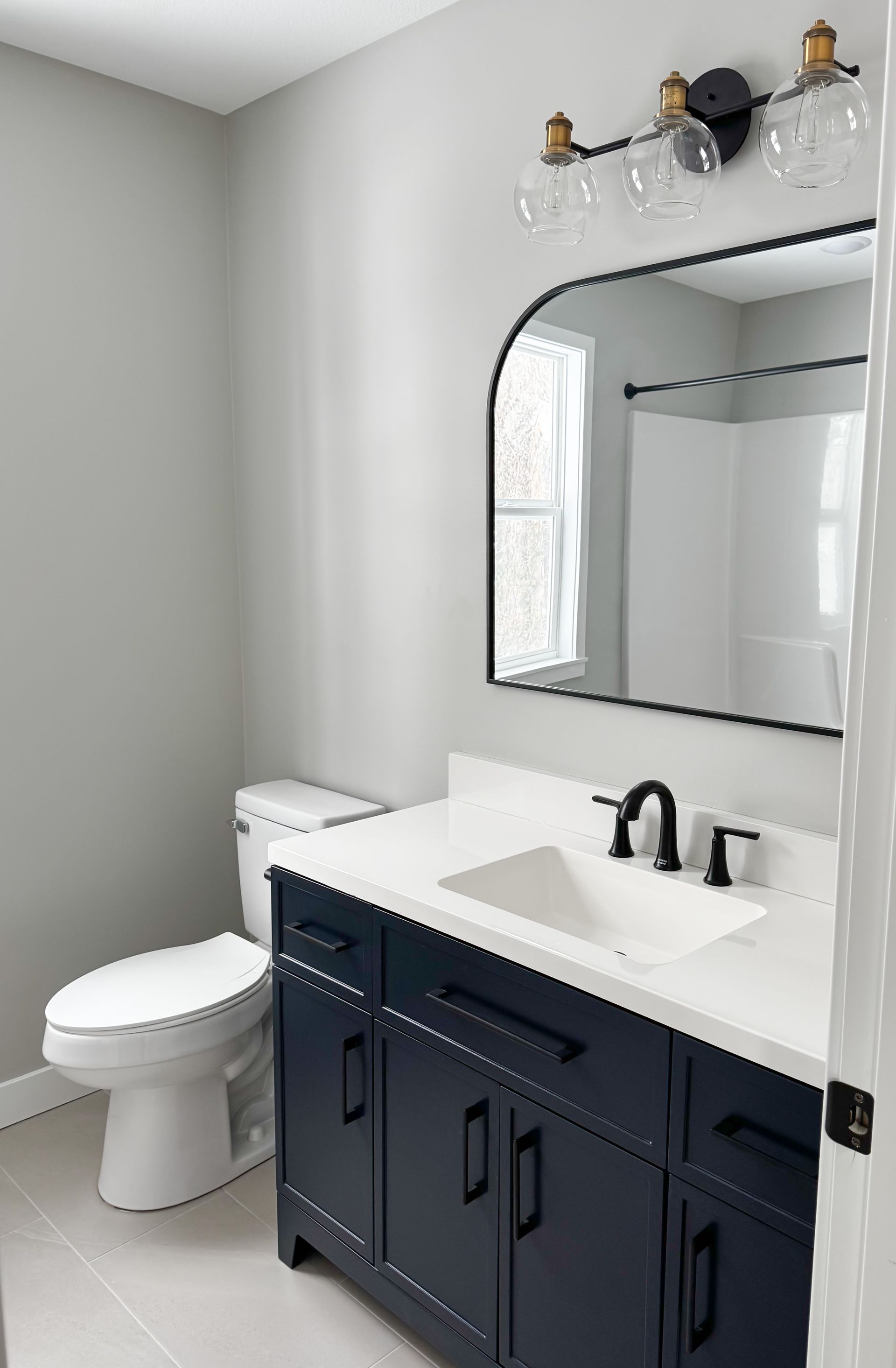 Modern bathroom with navy vanity, white sink, toilet, and mirror under wall sconce lights