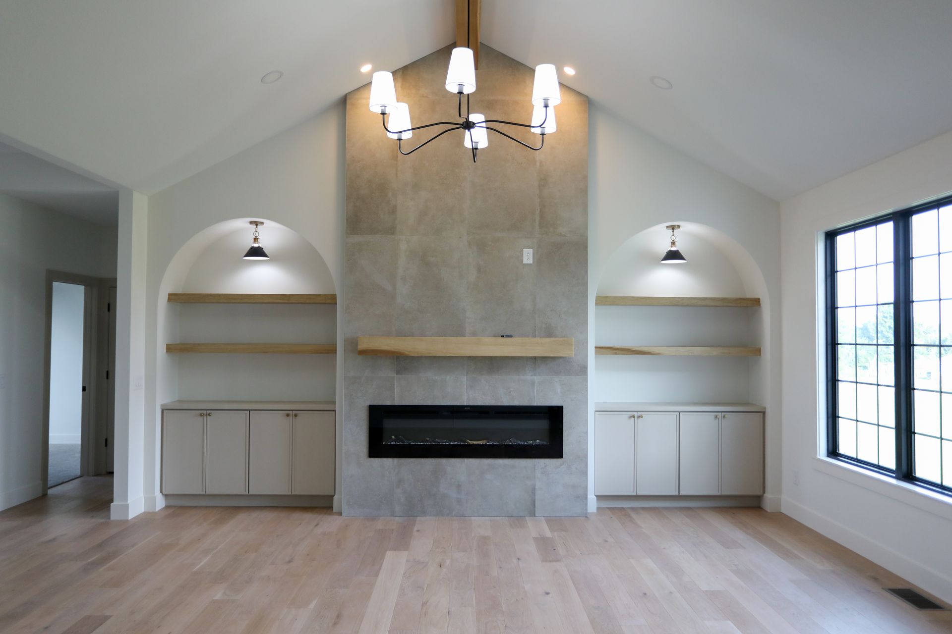Modern living room with a stone fireplace, built-in shelves, chandelier, and large window on the right.