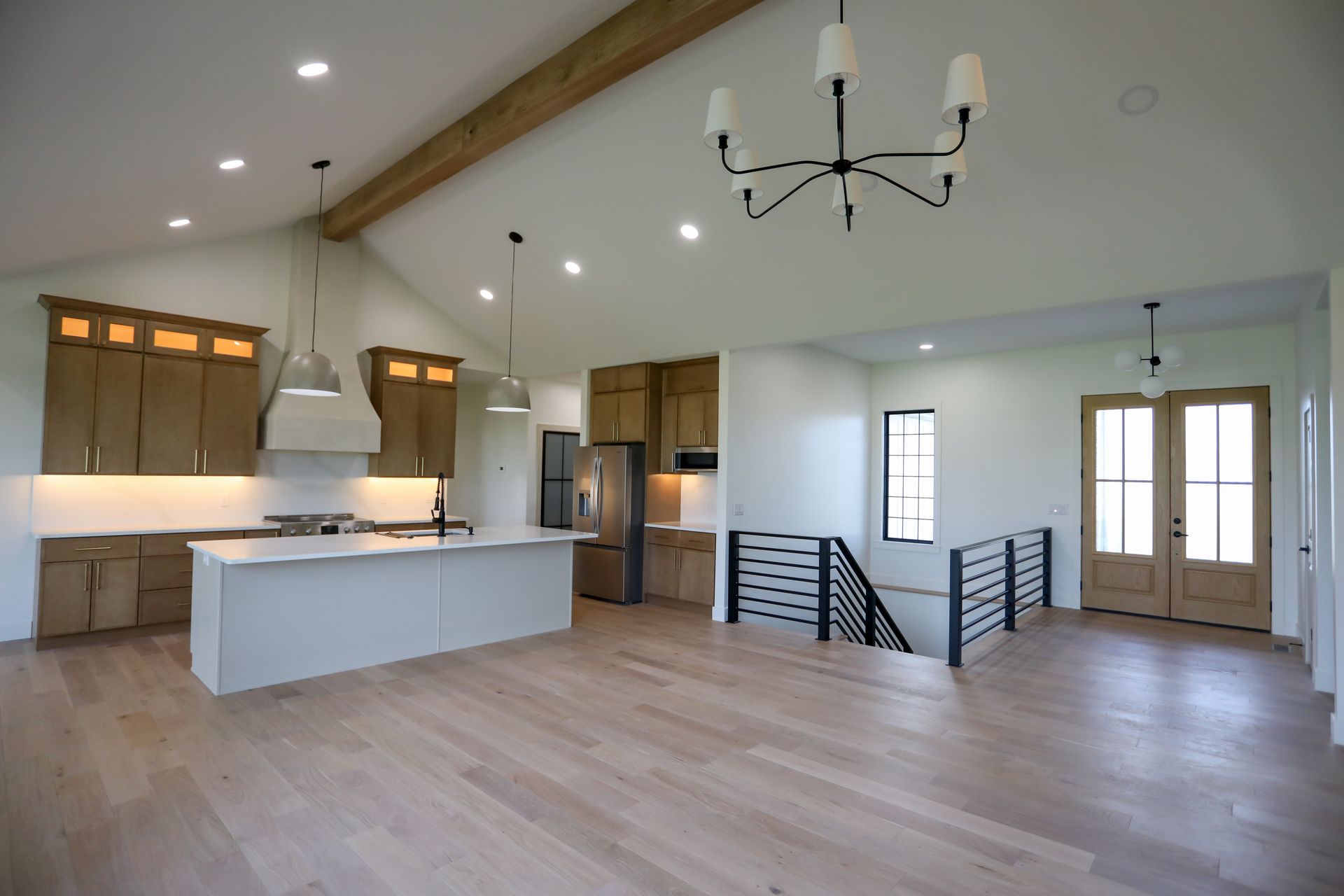 Bright open kitchen and living room with white island, wood floors, vaulted ceiling, and staircase.