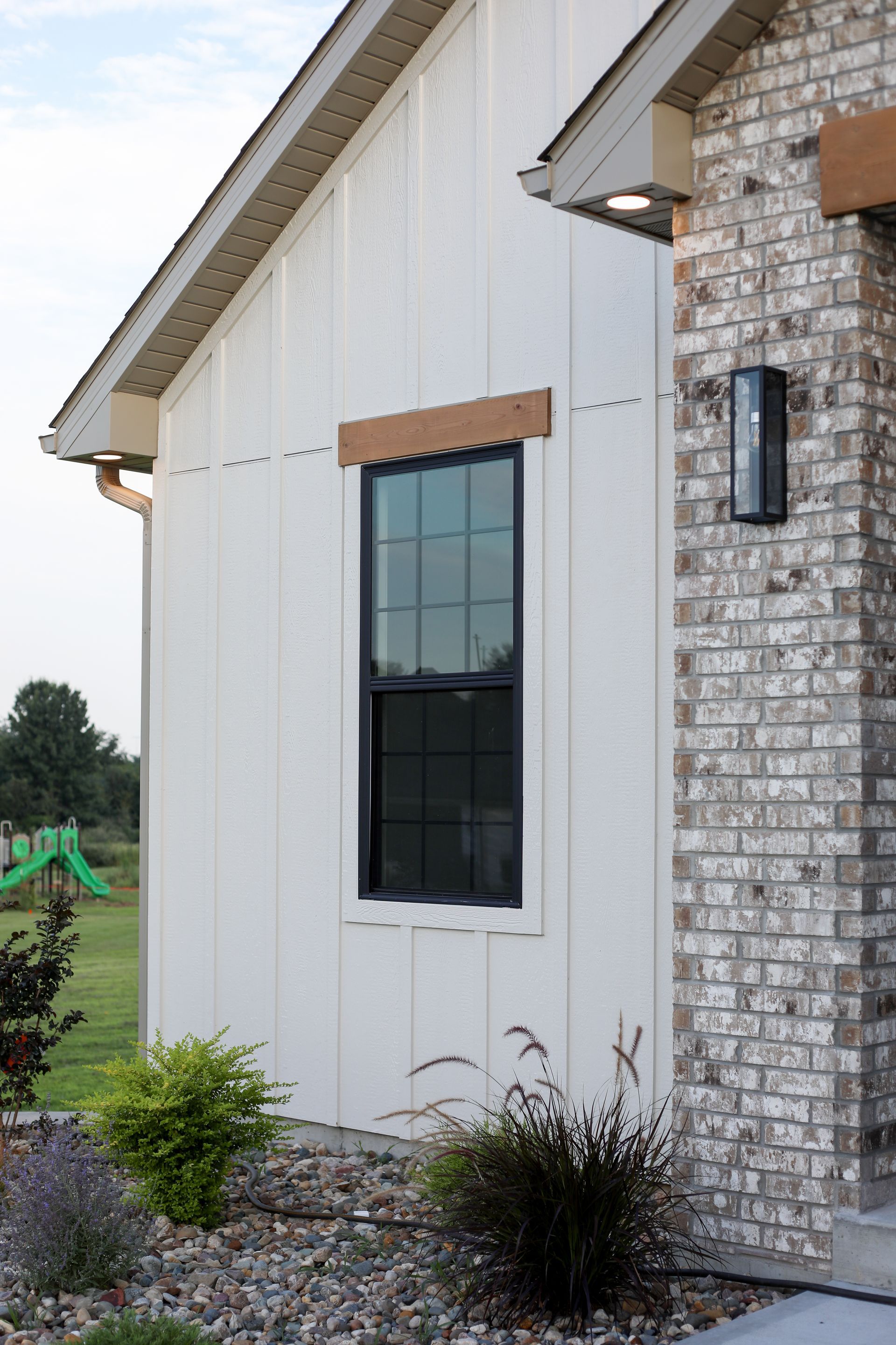 White brick house exterior with black window and small front landscaping