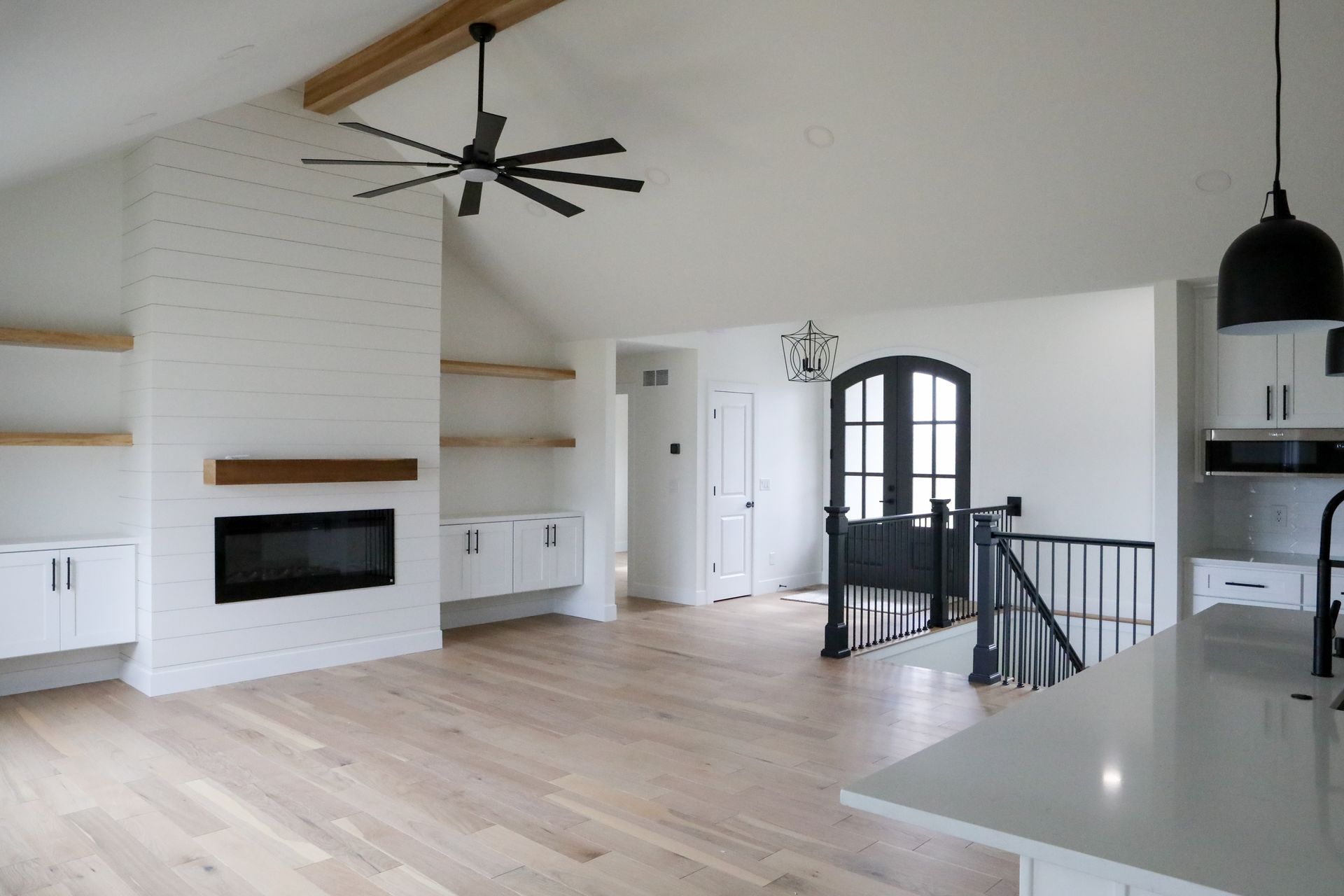 Modern open-concept living room with vaulted ceiling, fireplace, staircase, and dark front doors