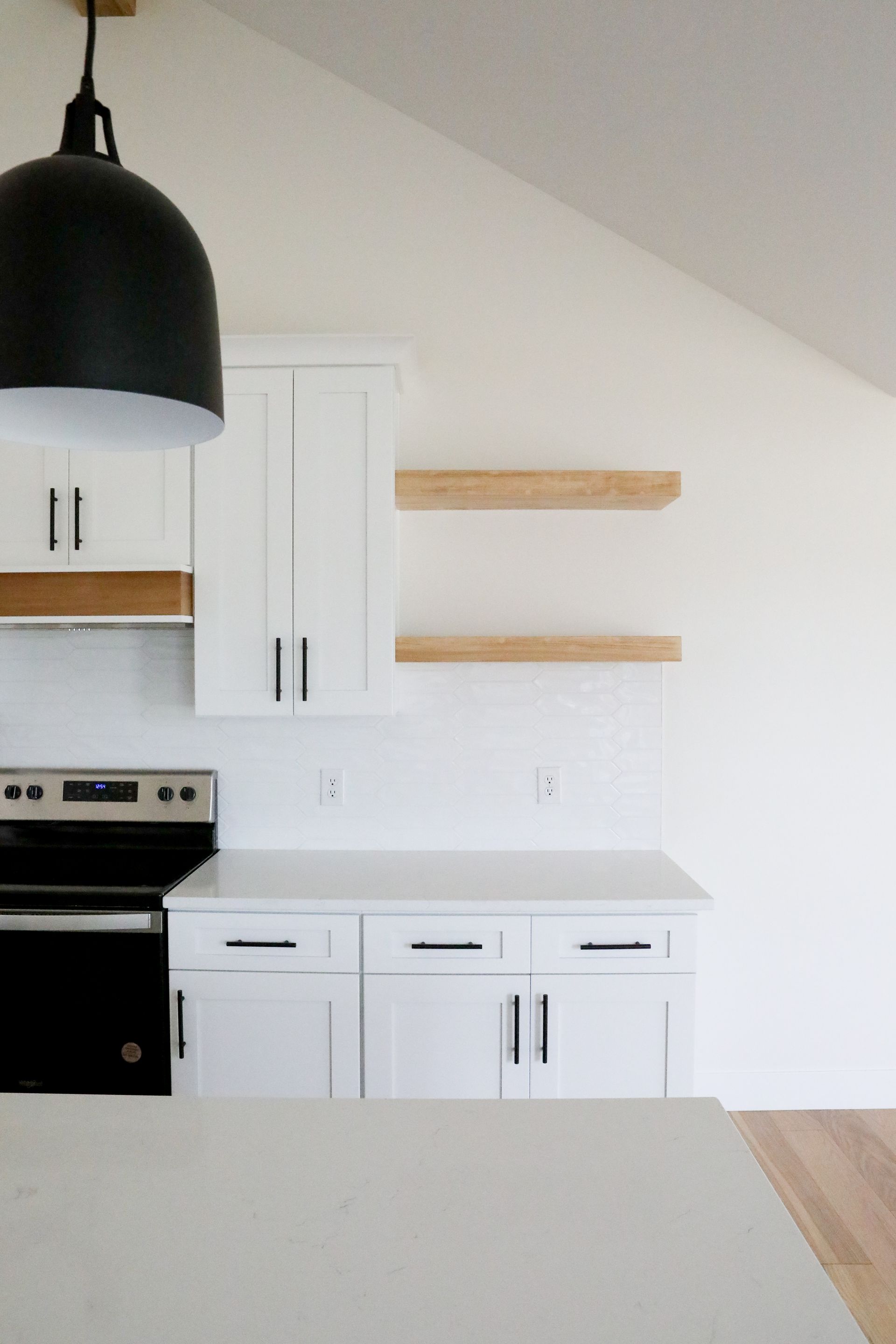 Minimal white kitchen with black pendant light and floating wood shelves