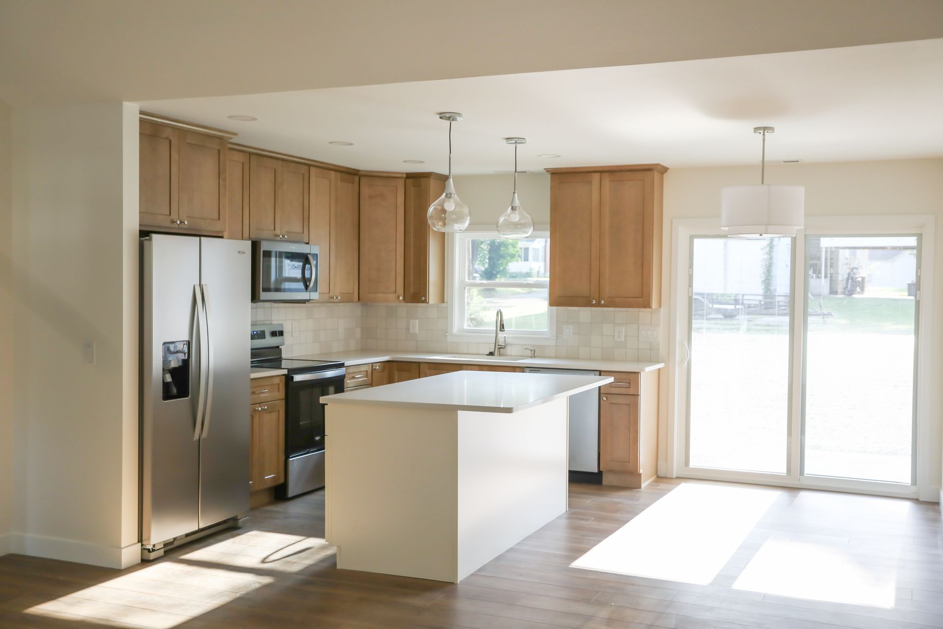 Bright kitchen with wood cabinets, white island, and sliding glass doors letting in sunlight.