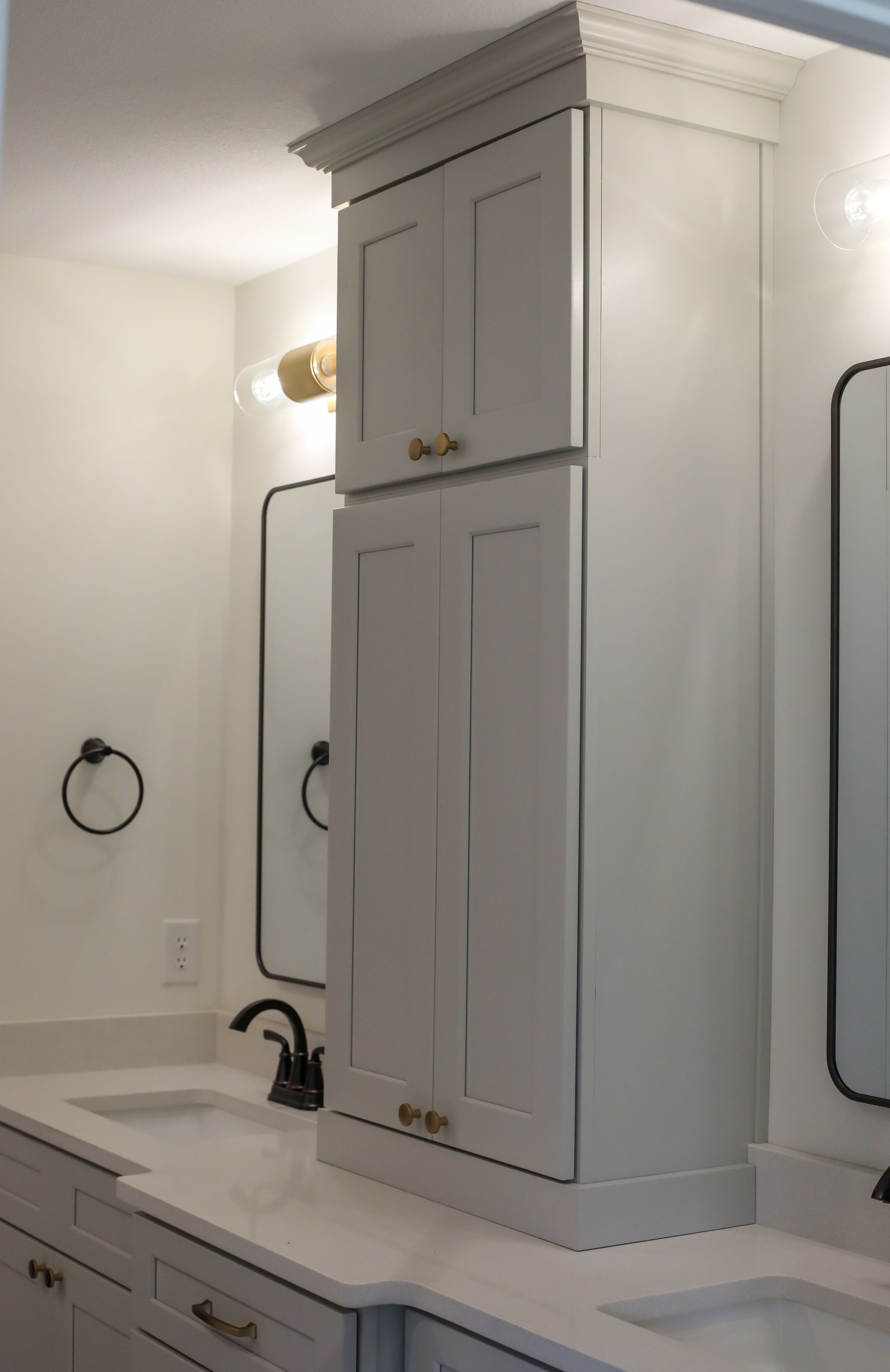 White bathroom vanity cabinet with mirrored side panels and wall sconce lighting above a sink and faucet.