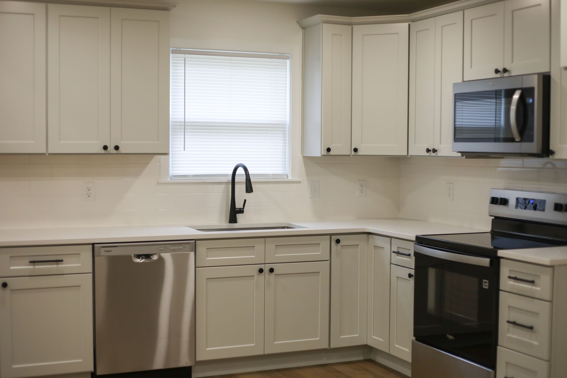 Modern white kitchen with stainless steel appliances, black countertops, and a window over the sink