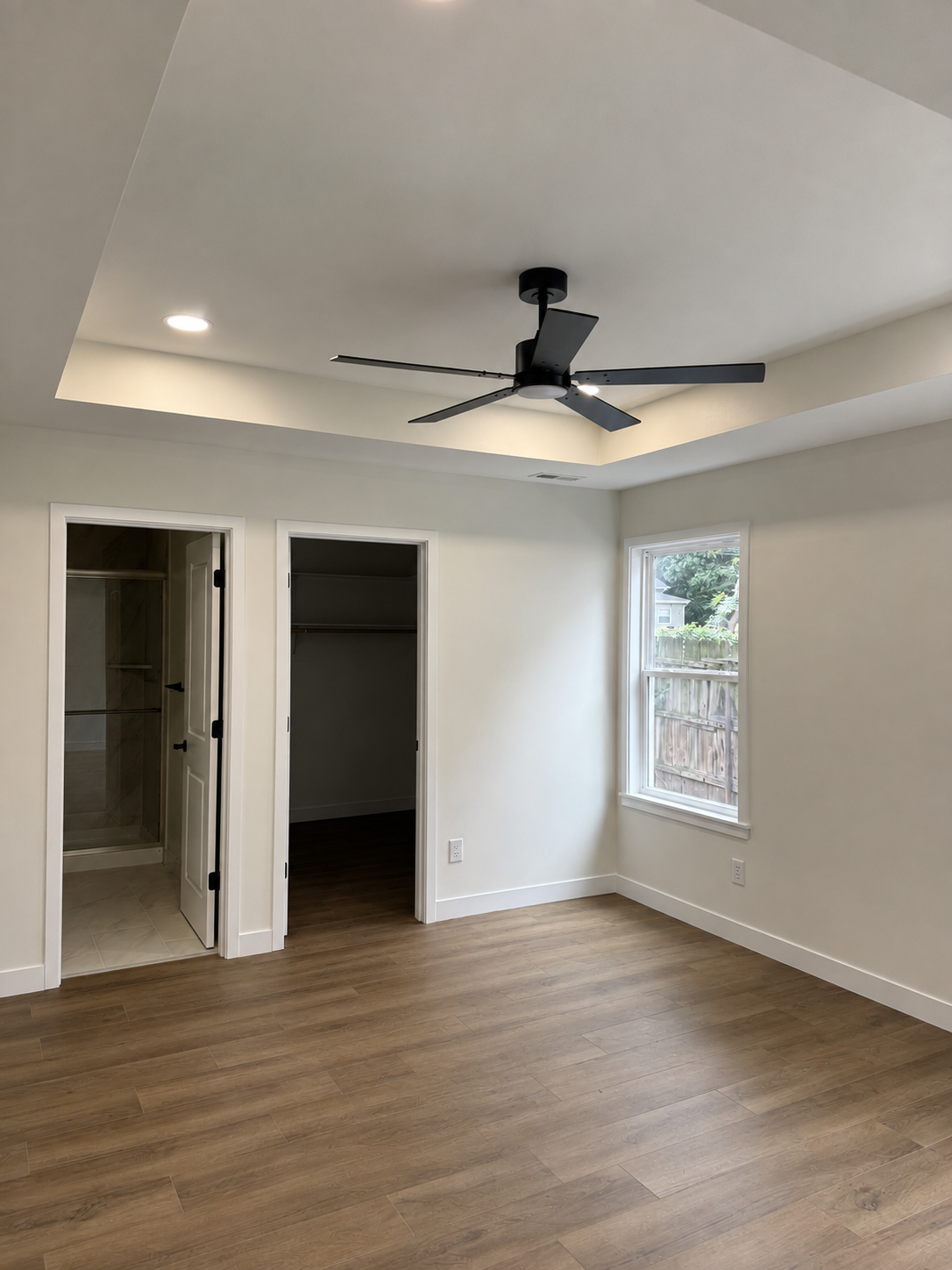Empty bedroom with wood floors, white walls, recessed lighting, ceiling fan, and open closet doors.
