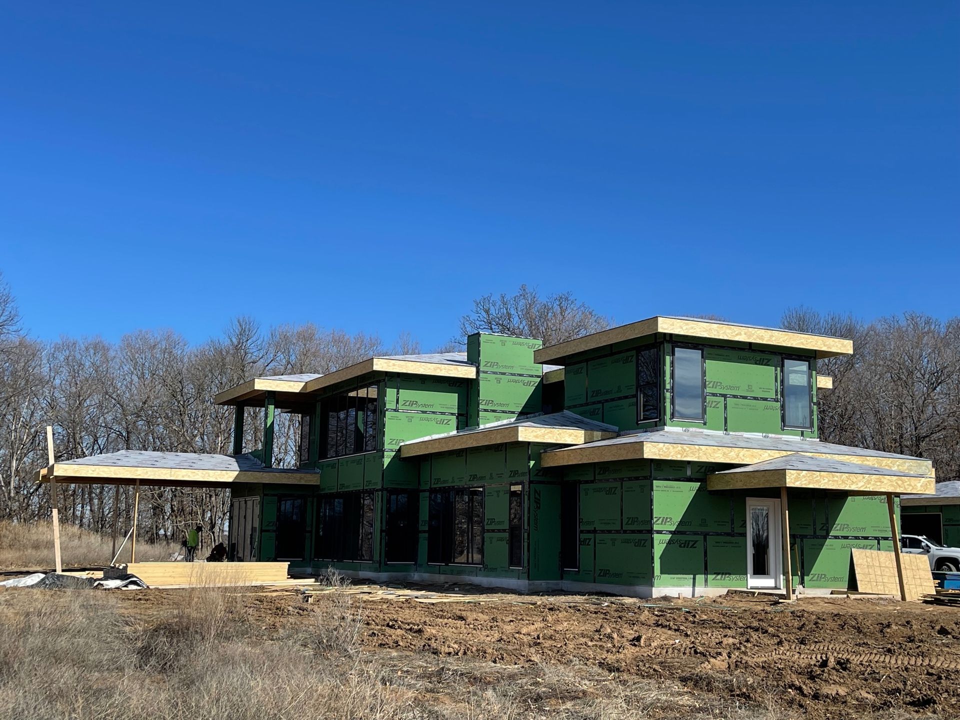 Green two-story house under construction on a dry lot beneath a clear blue sky