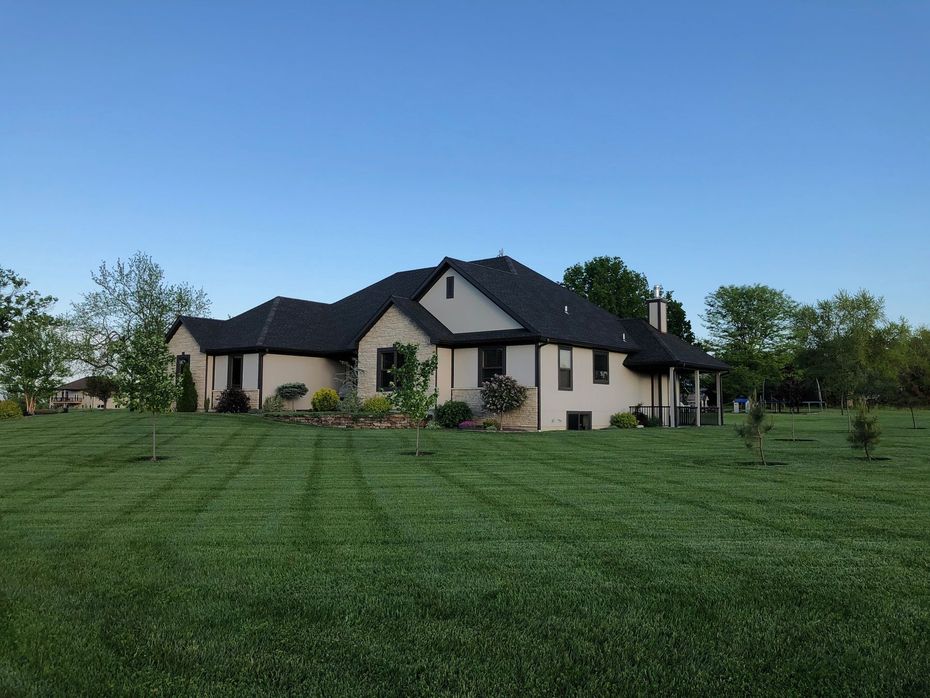 Large beige house with a dark roof on a green lawn under a clear blue sky