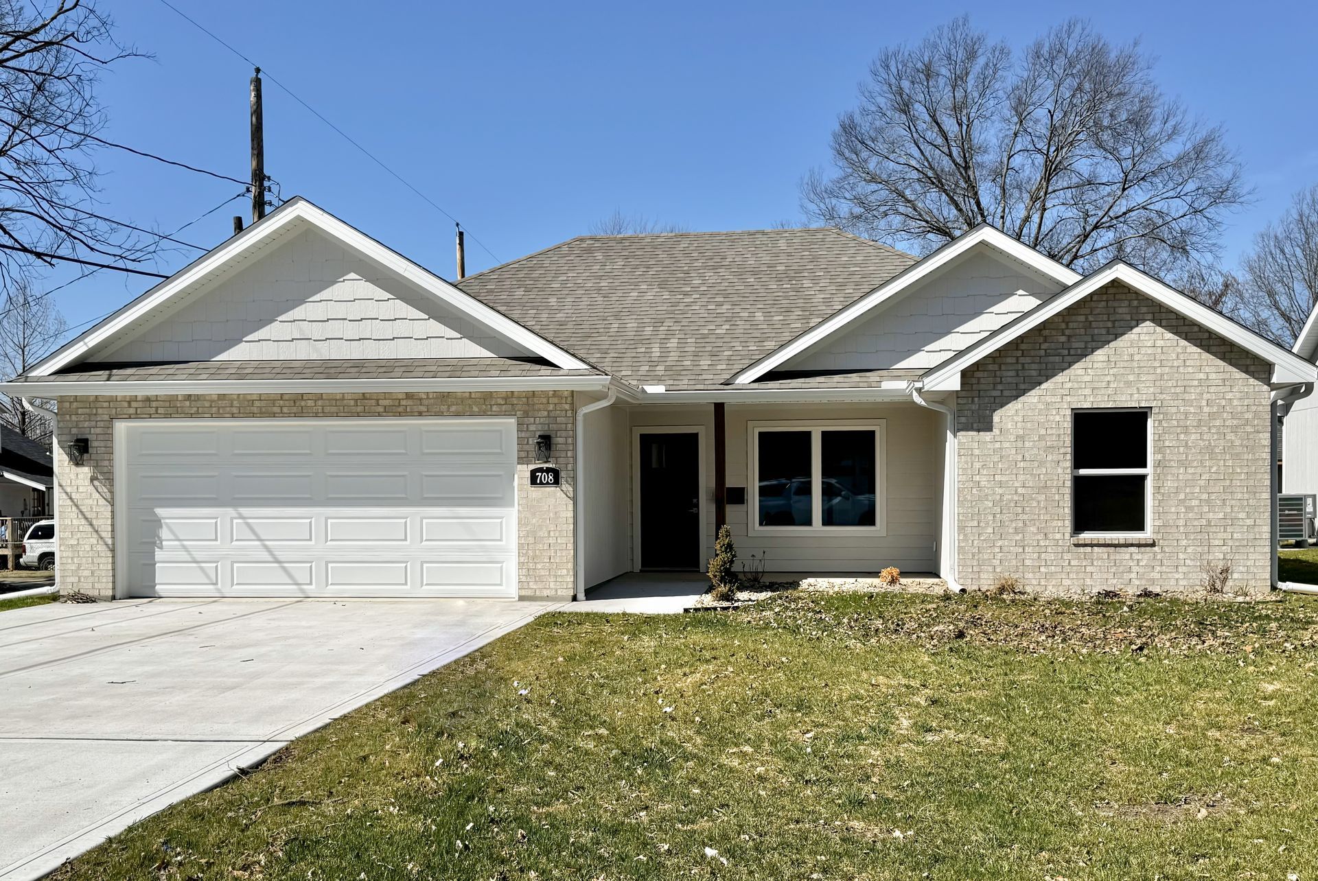 Single-story suburban house with a two-car garage, beige brick exterior, and front lawn under a blue sky