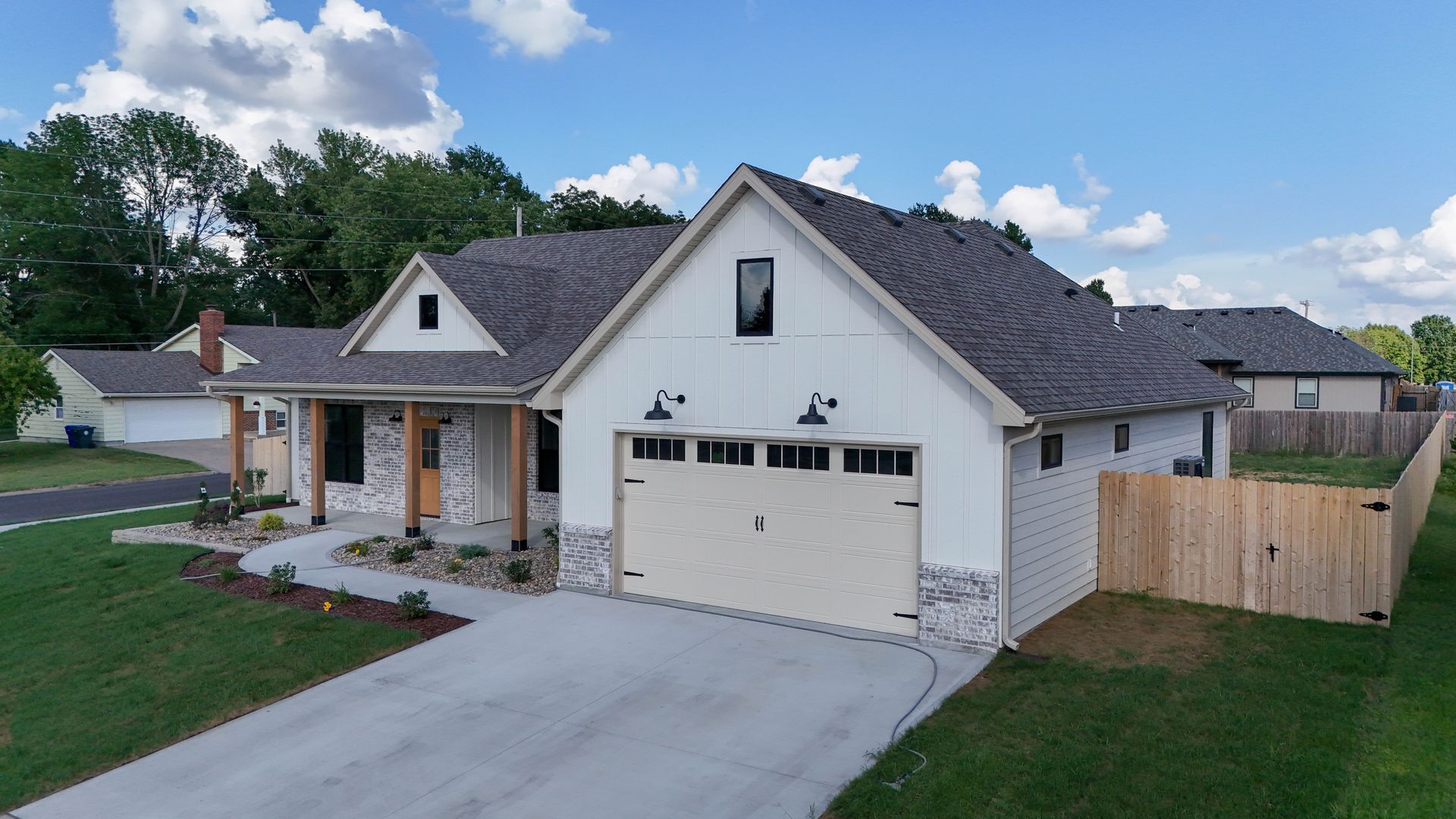 Modern white single-story house with a two-car garage, driveway, and fenced backyard under a blue sky