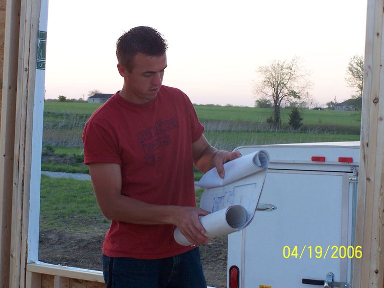 Man holding a rolled white tube beside a white trailer in a grassy field at sunset