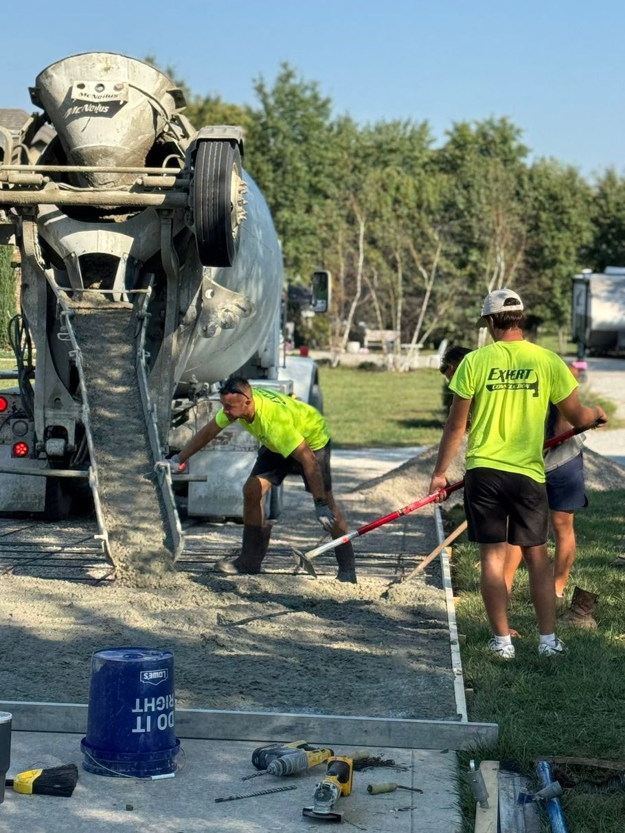 Concrete crew working beside mixer truck on a gravel road, pouring and leveling wet concrete.