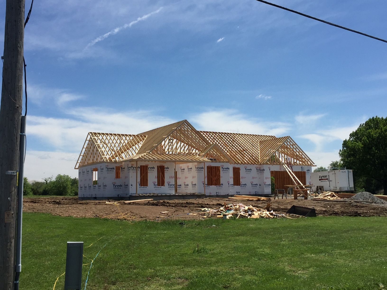 Partially built house with exposed roof framing on a dirt lot under a blue sky