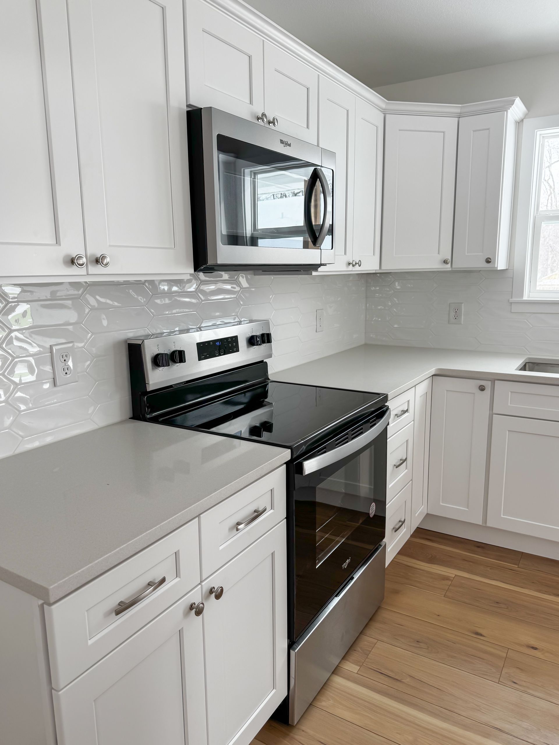 Modern white kitchen with stainless steel microwave and stove, white cabinets, and light wood floor