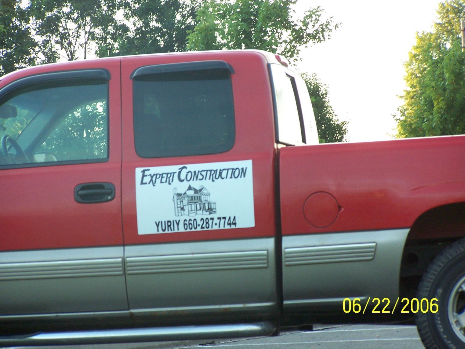 Red pickup truck with “Expert Construction” sign on door, parked outdoors.