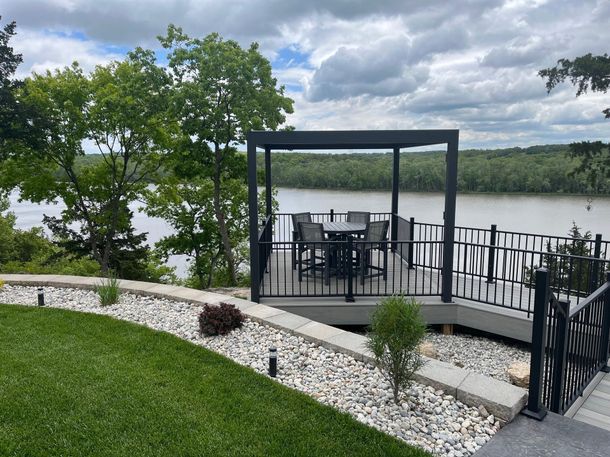 Backyard patio with black pergola and dining set overlooking a lake under cloudy skies