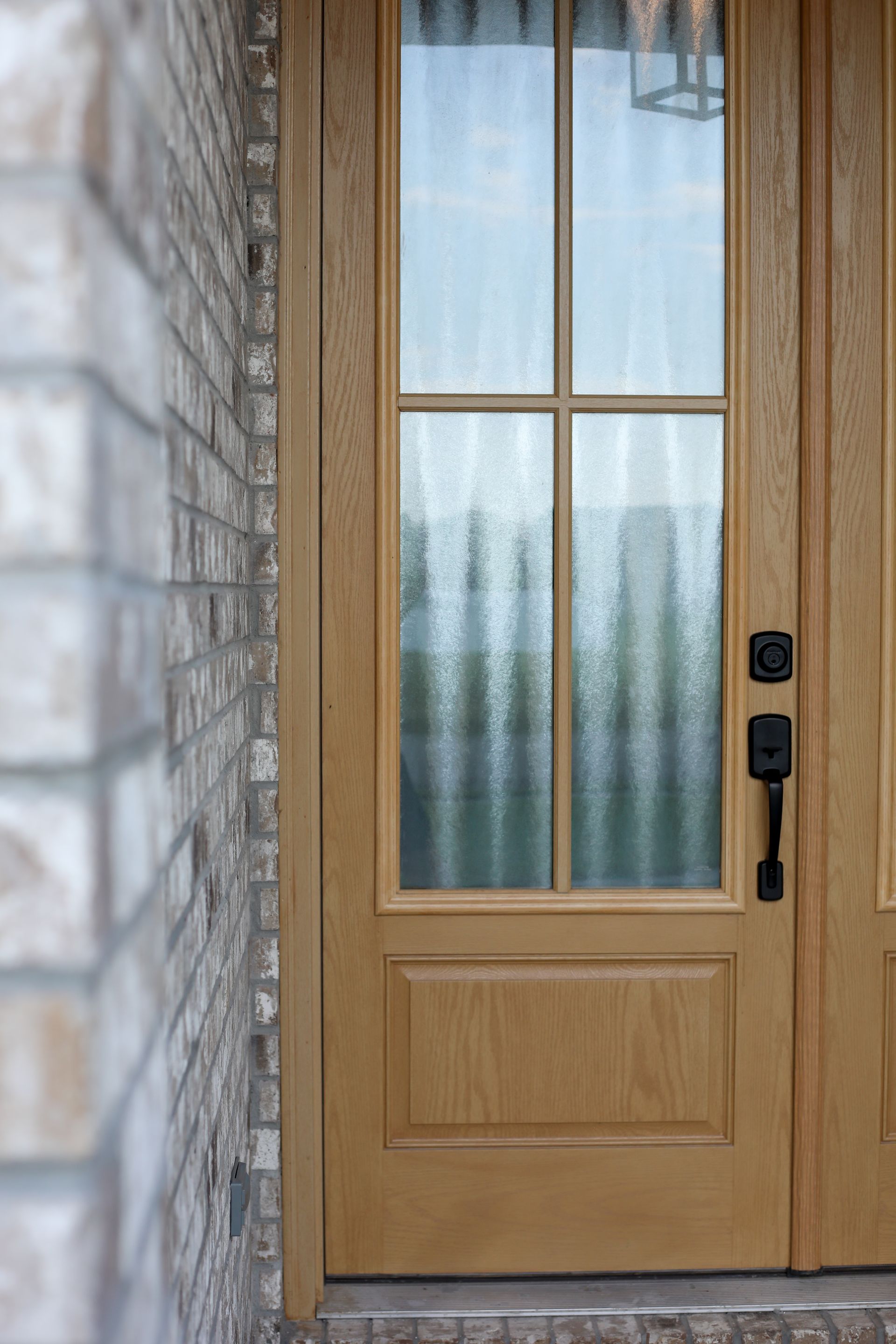 Wooden front door with glass panes and black handle beside a stone wall