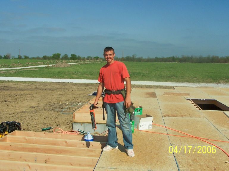 Man standing at a construction site beside lumber and tools under a clear sky.