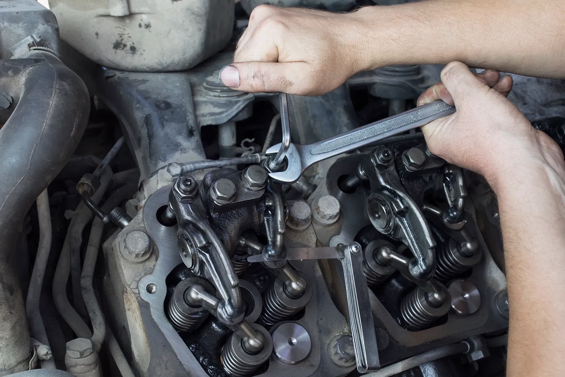 Mechanic using a wrench to adjust engine valves under an open car hood — Bundaberg Field Service in Bundaberg East, QLD