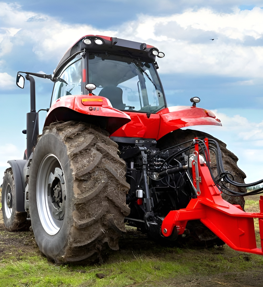 Red Tractor with Large Muddy Tires and Front Mower Attachment in A Field — Bundaberg Field Service in Bundaberg East, QLD
