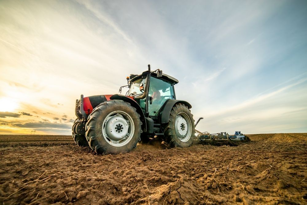 Tractor plowing a field at sunset under a dramatic sky — Bundaberg Field Service in Gin Gin, QLD