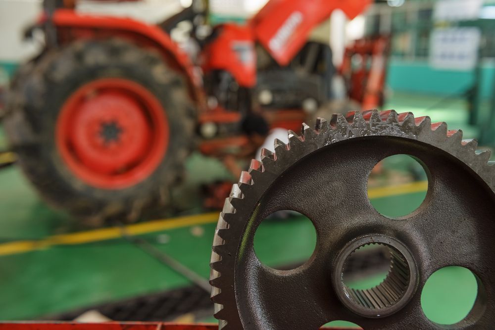 Close Up of A Rusty Gear Wheel with A Red Tractor Blurred in The Background — Bundaberg Field Service in Agnes Waters, QLD