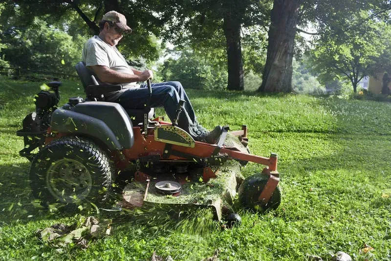 Person mowing a grassy field on a riding lawn mower in a park-like setting — Bundaberg Field Service in Woodgate, QLD