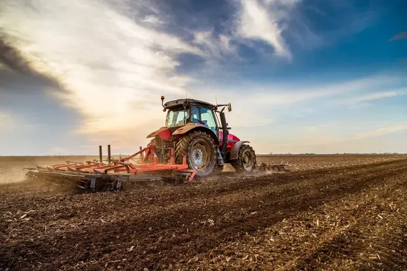 Red tractor plowing a brown field under a cloudy sunset sky — Bundaberg Field Service in Woodgate, QLD