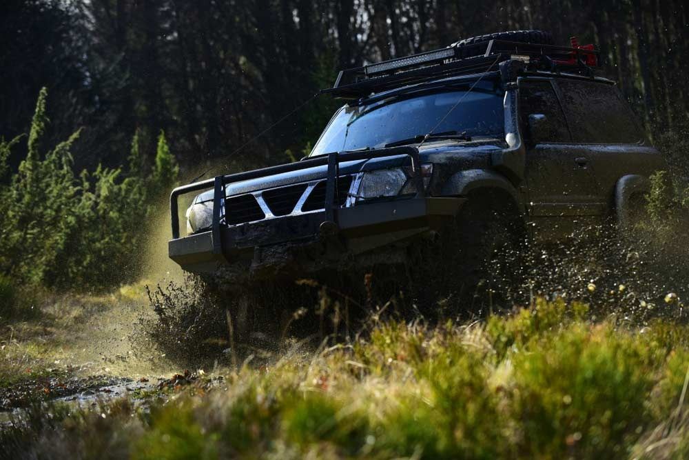 Dark off-road truck splashing through muddy grass in a forest trail — Bundaberg Field Service in Woodgate, QLD