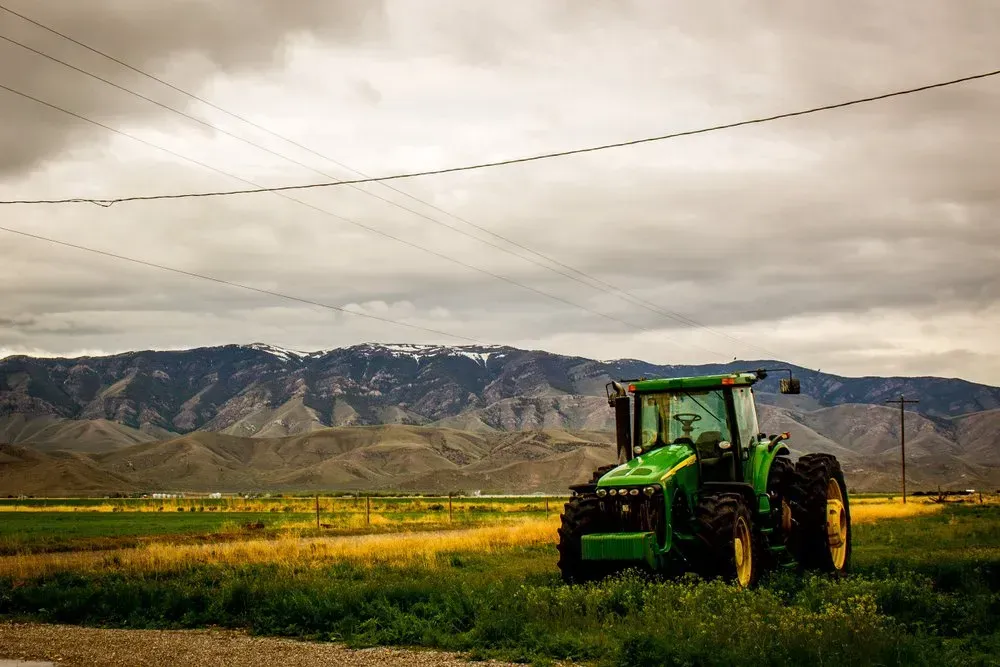 Green tractor in a field with mountains and cloudy sky in the background — Bundaberg Field Service in Bundaberg East, QLD
