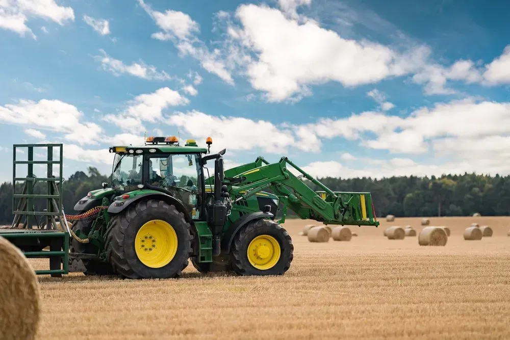 Green tractor with front loader in a hay field, baling hay under a partly cloudy sky — Bundaberg Field Service in Bundaberg East, QLD