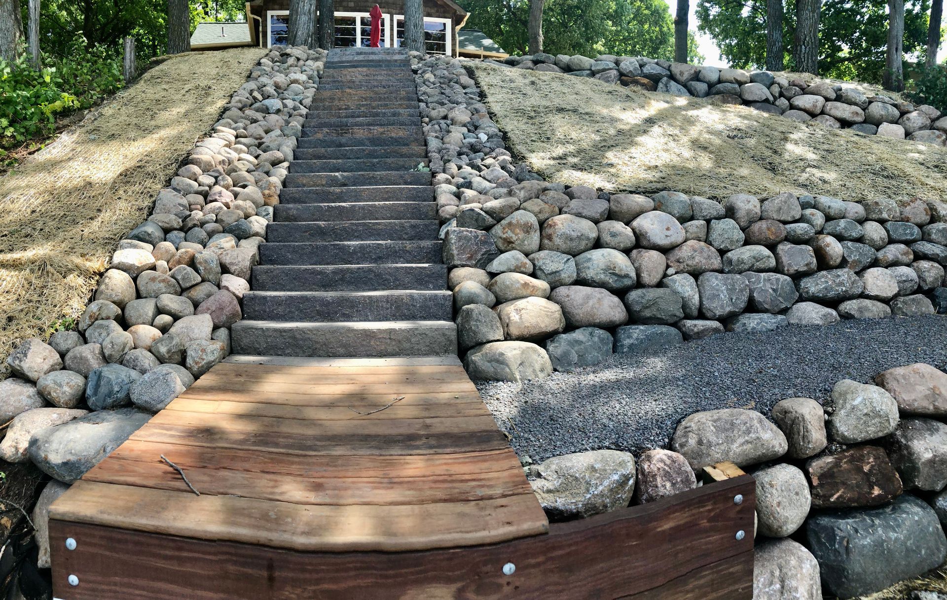 Stone staircase leading up a landscaped hillside with rock retaining walls and trees