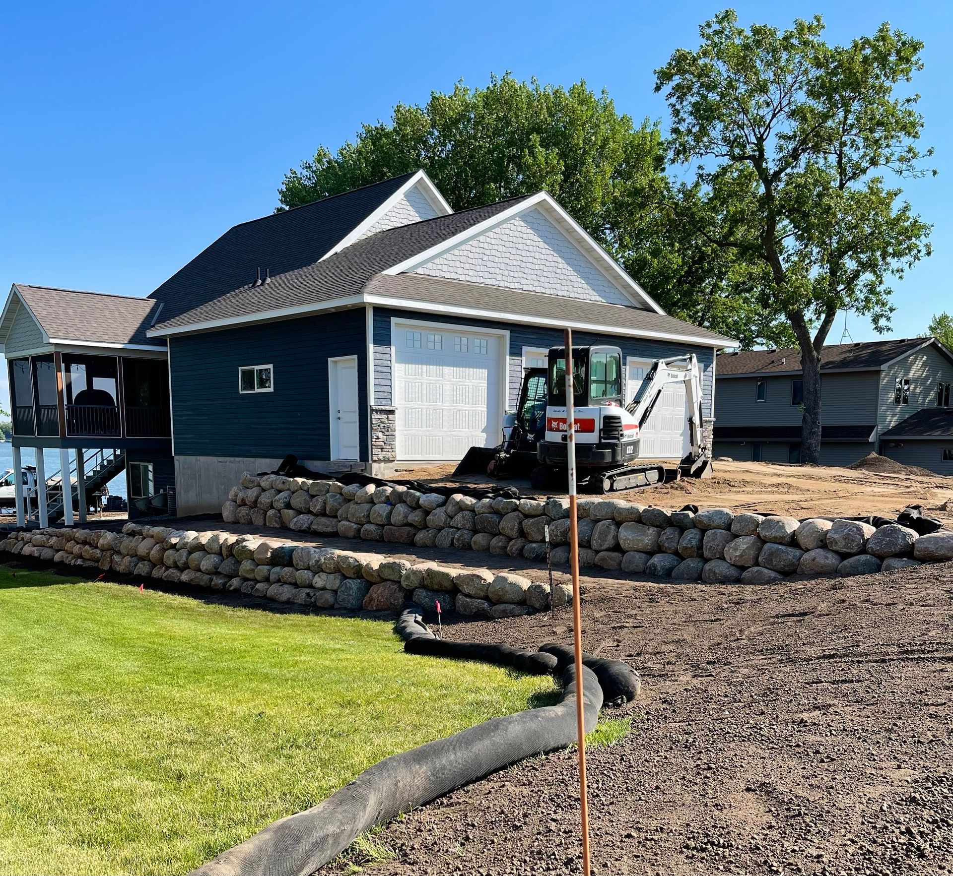 Modern house with stone retaining wall, driveway, and a parked pickup truck on a sunny day