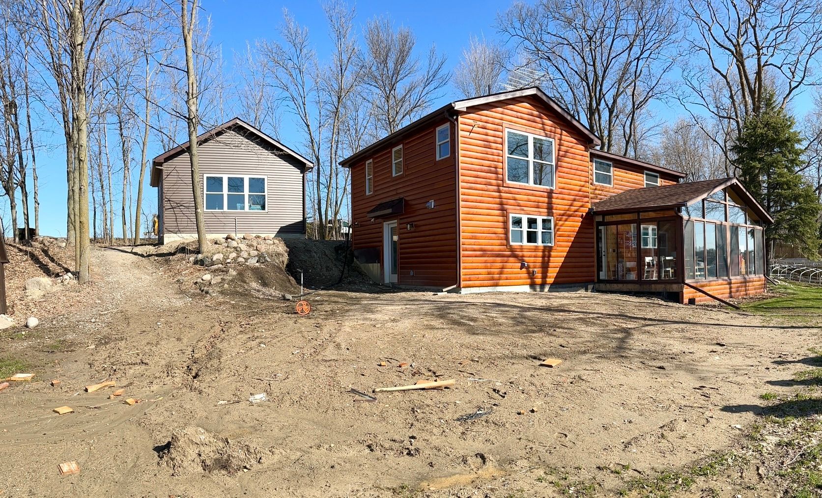Two small cabins on a wooded hillside, one orange and one beige, under clear blue sky
