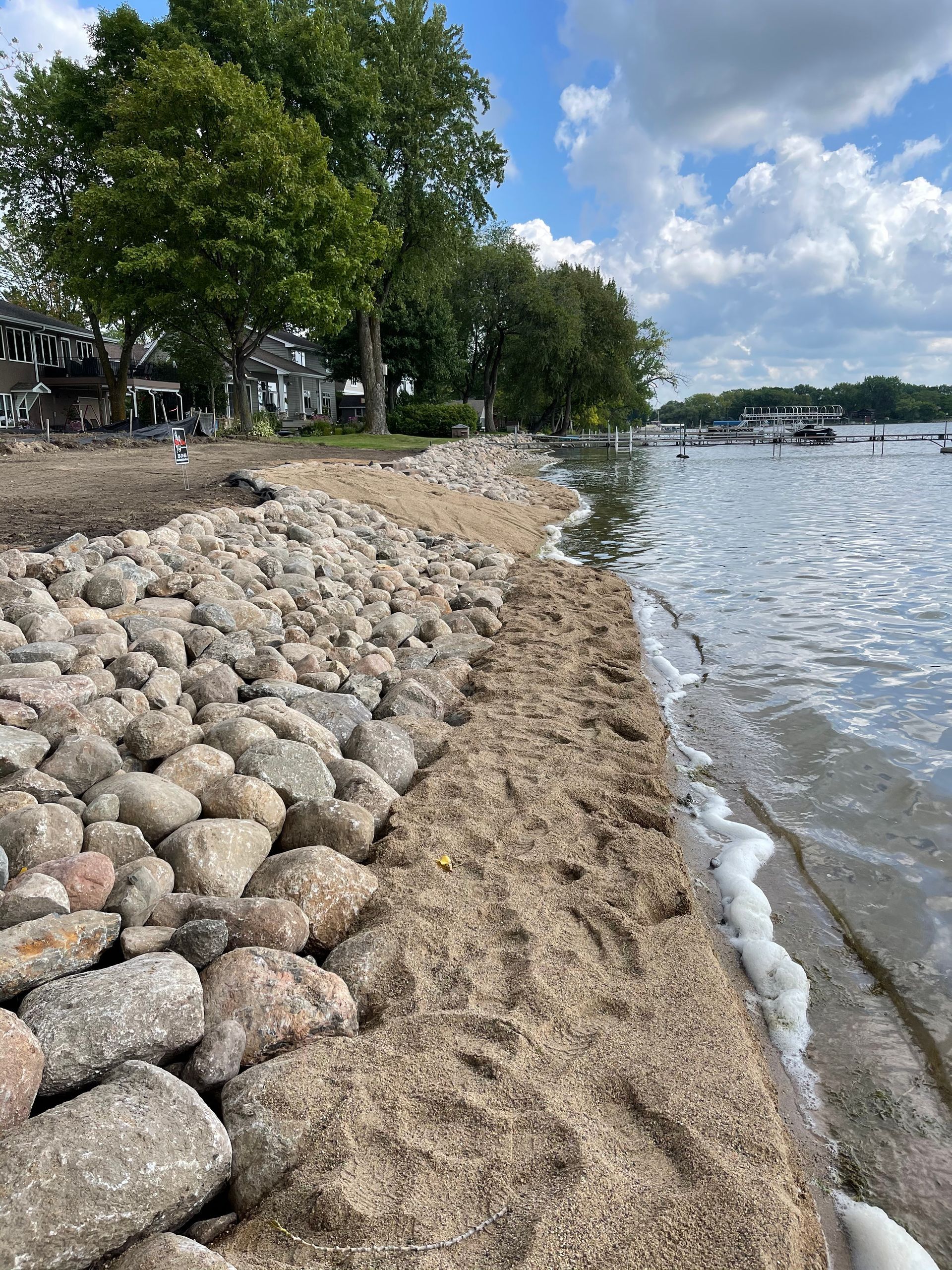 Rocky shoreline with trees beside a calm lake under a partly cloudy sky