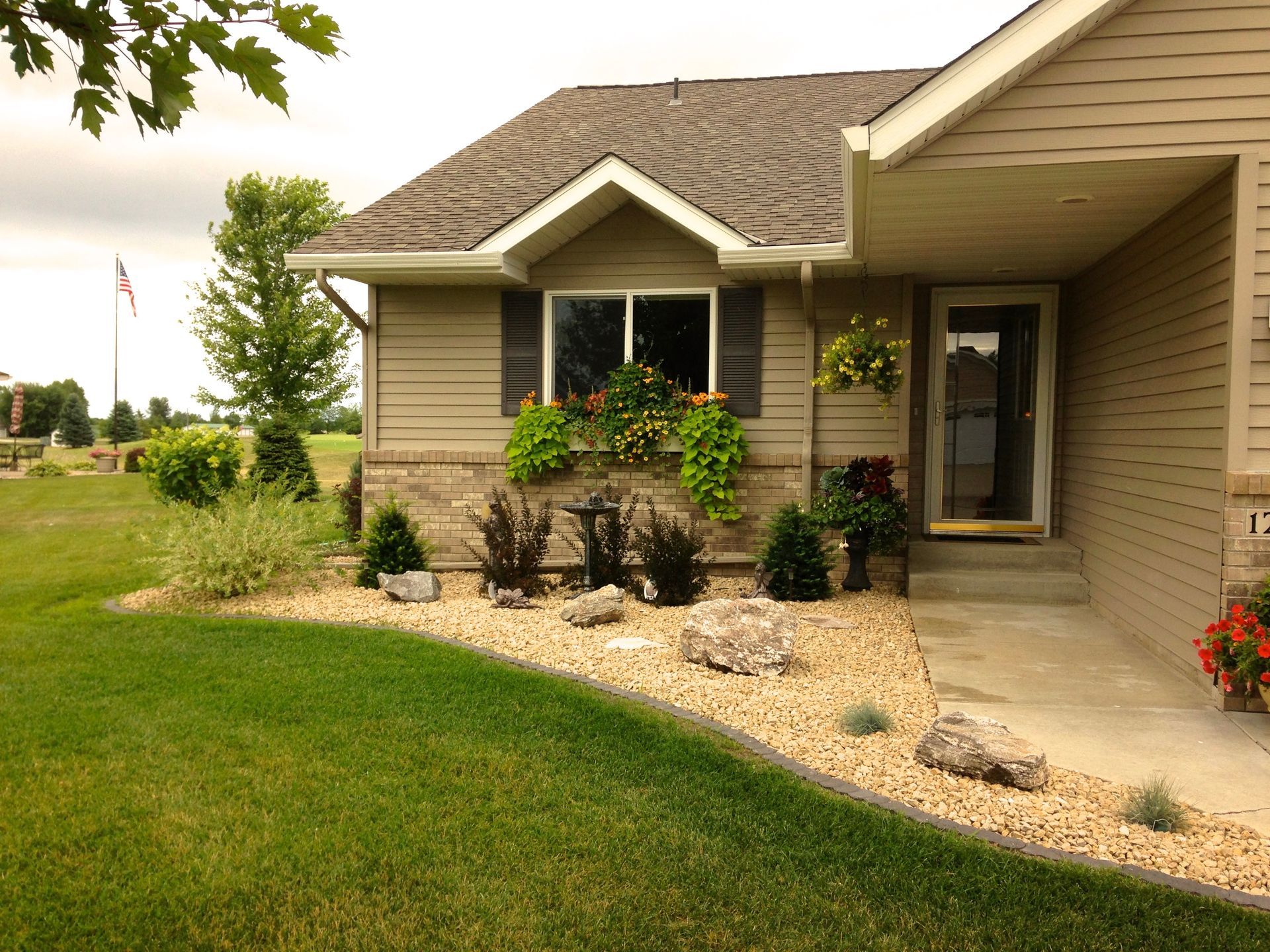 Suburban house with beige siding, front porch, and landscaped rock garden beside a green lawn